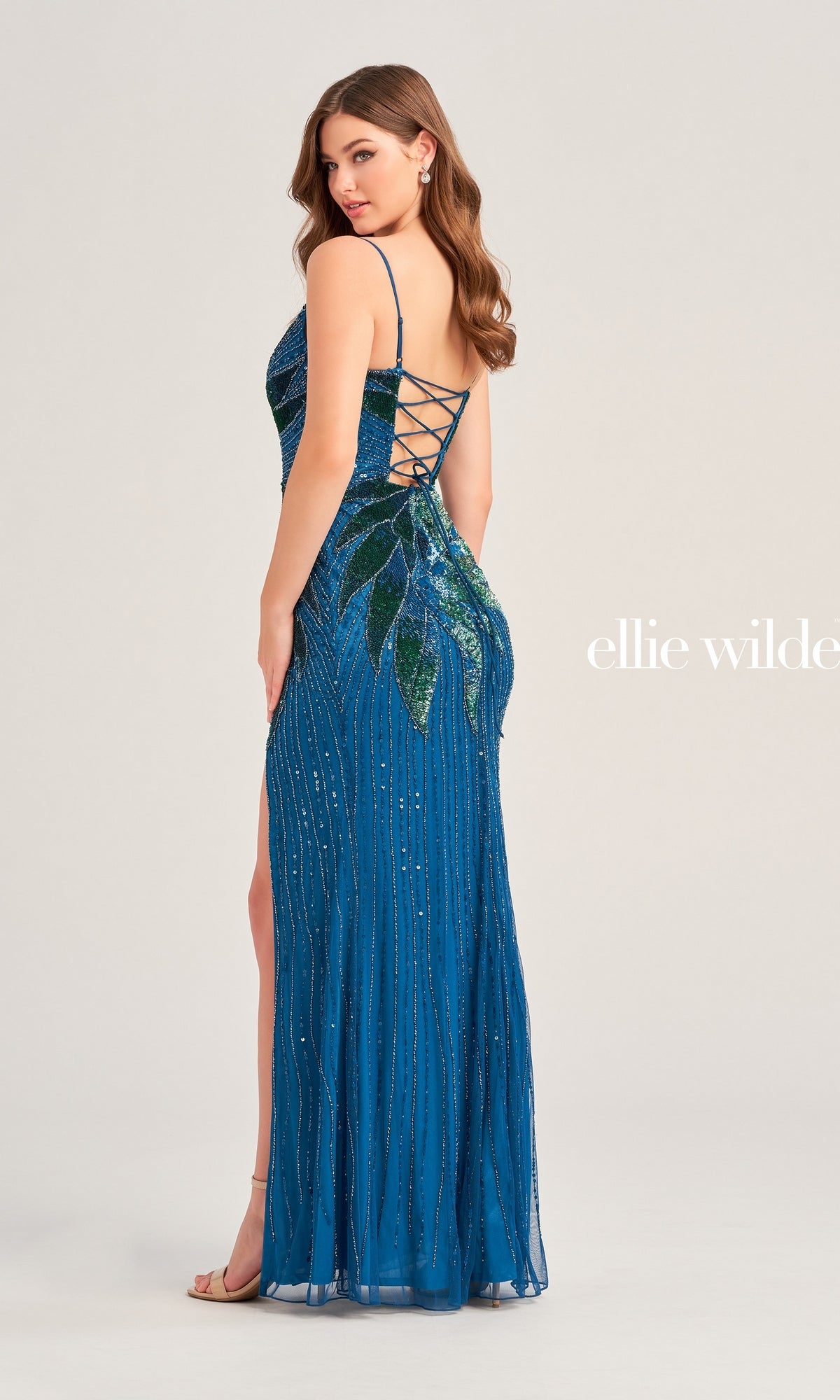 A woman in a blue Two-Tone Ellie Wilde Beaded Prom Dress EW35066 with sequin details and lace-up back stands sideways against a plain background.